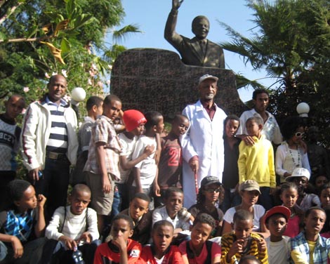 ሰዓሊው የሁለት አፍሪካዊ ጓደኛሞችን የፎቶ ምስል በመሳል ሥራ ላይ እያሉ ሰዓሊ ሻምበል ለማ ጉያ ማዕከሉን ለመጎብኘት ከስኩል ኦፍ አይጎዳ ከአዲስ አበባ ከመጡ ተማሪዎች ጋር